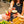 Load image into Gallery viewer, There is a lady in the background, although you cannot see her head (it&#39;s Danni btw! The founder!) She is holding a lychee martini and toasting with two other people. They are holding an espresso martini and a raspberry collins. All three people are sitting outside on a tall wooden table, and a flower pot is on the table with bright yellow flowers.
